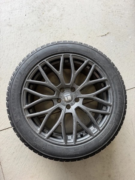 Winter tire mounted on a grey mesh-spoke alloy wheel, lying flat on a concrete floor